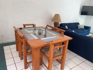 A dining table with chairs, a blue sofa, and a lamp in a room with white walls and tiled flooring. - Monthly Beach House Rental in Manzanillo, Mexico – Perfect for Snowbirds (Manzanillo)