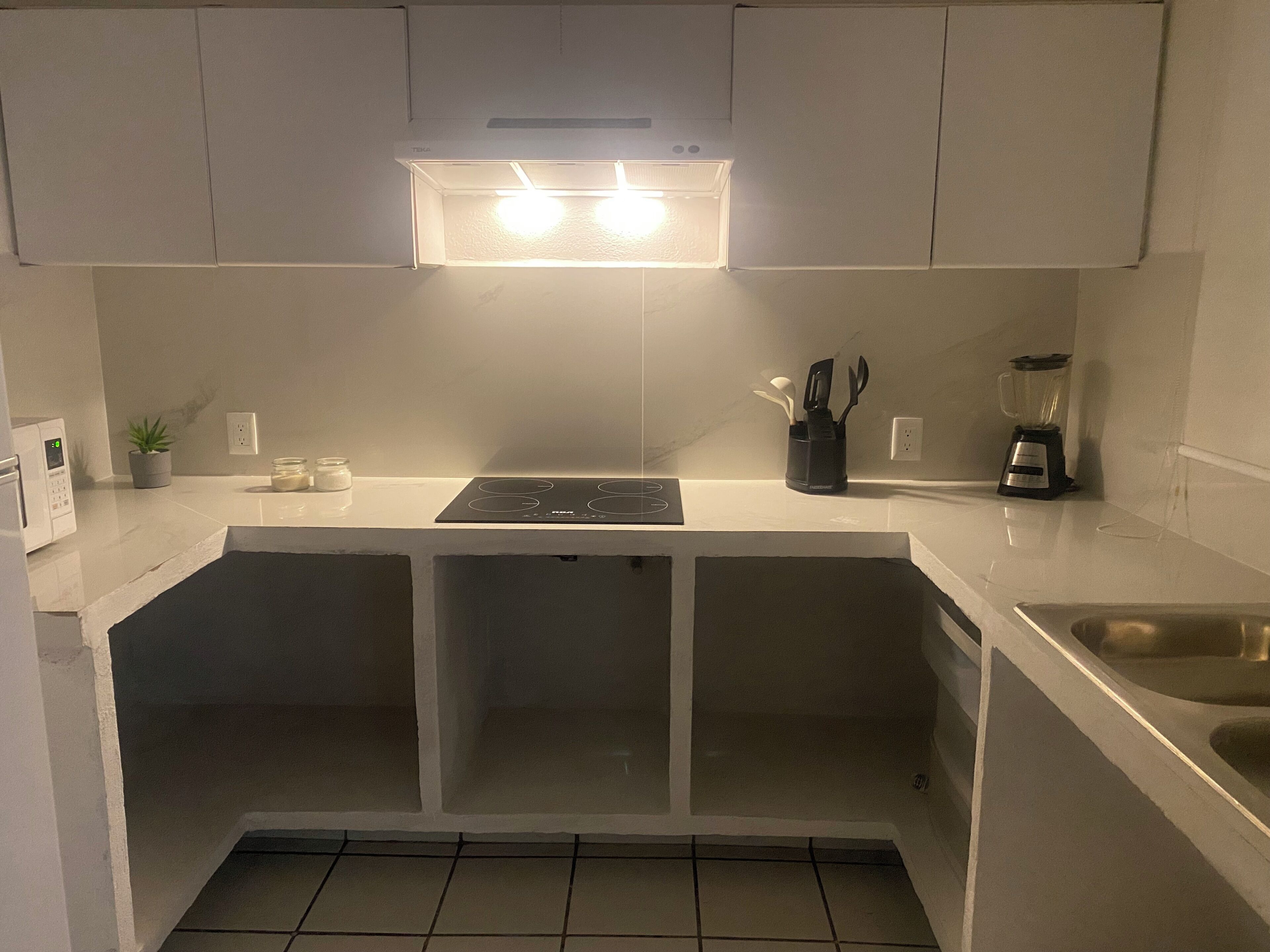 A kitchen with white cabinets, a built-in stove, a microwave, a blender, and a sink.