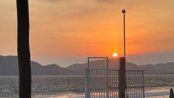 Un espace aménagé au bord de la piscine, avec des chaises et une table, d’où l’on peut admirer un plan d’eau et un coucher de soleil en arrière-plan.