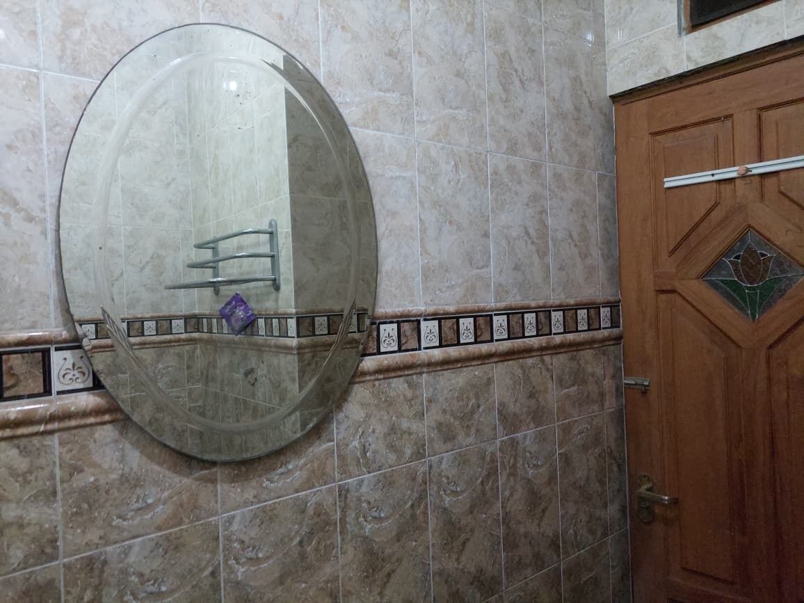 A bathroom with a large mirror, a wooden door, and a tiled wall.