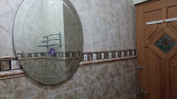 A bathroom with a large mirror, a wooden door, and a tiled wall.