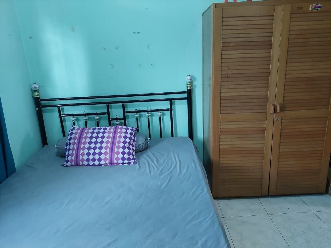 A single bed with a metal headboard and a patterned pillow, a wooden wardrobe, and a tiled floor.