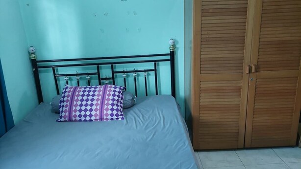 Una cama individual con cabecera de metal y un cojín estampado, un armario de madera y un suelo de baldosas.