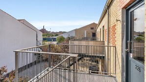 Un pati amb una escala metàl·lica que condueix a una entrada tancada per una reixa, envoltat d'edificis amb façanes de maó i un cel serè.