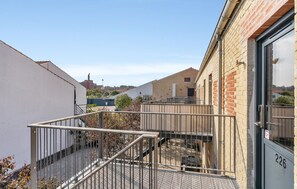 Ein Innenhof mit einer Metalltreppe, die zu einem verschlossenen Eingang führt, umgeben von Gebäuden mit Backsteinfassaden und blauem Himmel.