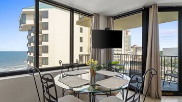 A balcony with a glass table and chairs, a flat-screen TV, and a view of the ocean.