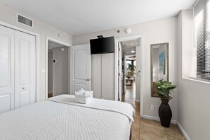 Ein Schlafzimmer mit einem Bett, einem an der Wand montierten Fernseher, einer Tür und einem Fenster mit Jalousien.