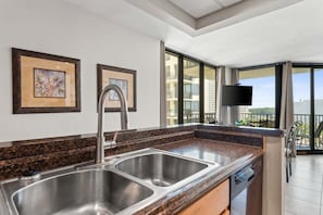 A modern kitchen with two stainless steel sinks, a granite countertop, and a large window overlooking a balcony. - Renovated Beachfront, Gulf Views & 3 Pools | Sunbird 912E (Panama City)