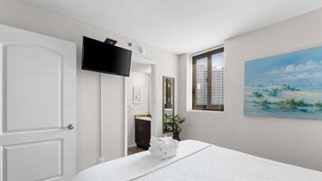 A hotel room with a bed, a television, a painting, and a window with blinds.