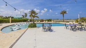 Zona de piscina amb gandules i taula, envoltada de palmeres i un cel serè.