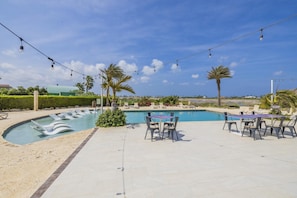 A swimming pool area with lounge chairs and a table, surrounded by palm trees and a clear sky. - Stylish Gold Coast 1BR  Near Beach  Pools & Gym (Noord)