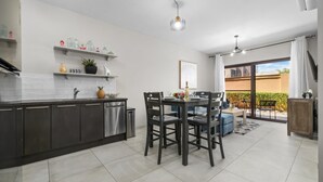 Una cuina moderna amb armaris foscos, una zona de menjador amb taula i cadires, i una porta corredissa de vidre que dona a un pati exterior.