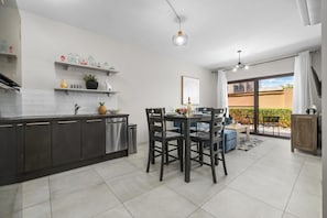 A modern kitchen with dark cabinets, a dining area with a table and chairs, and a sliding glass door leading to an outdoor patio. - Stylish Gold Coast 1BR  Near Beach  Pools & Gym (Noord)