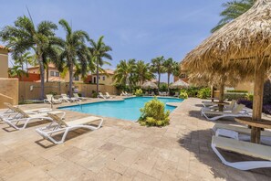 A poolside area with lounge chairs, a swimming pool, palm trees, and thatched umbrellas. - Stylish Gold Coast 1BR  Near Beach  Pools & Gym (Noord)