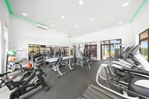 A modern gym with various exercise machines, a mirrored wall, and large windows offering natural light. - Stylish Gold Coast 1BR  Near Beach  Pools & Gym (Noord)