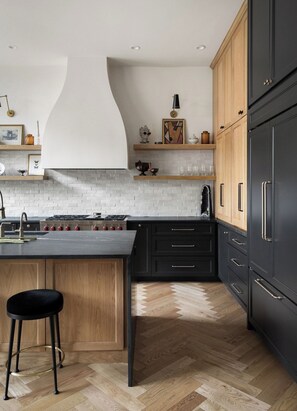 Eine moderne Küche mit einer zentralen Kochinsel, Holzschränken und einem schwarzen Kühlschrank.