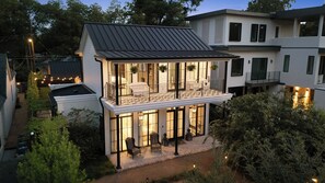 A two-story house with a balcony, large windows, and a well-lit exterior. - Award Winning. East Austin. Pool. Speakeasy. 1 mi from DT. Events & photoshoots (Austin)