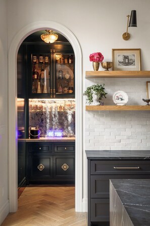 A kitchen with a black cabinet, a white brick wall, and a shelf with decorative items. - Award Winning. East Austin. Pool. Speakeasy. 1 mi from DT. Events & photoshoots (Austin)