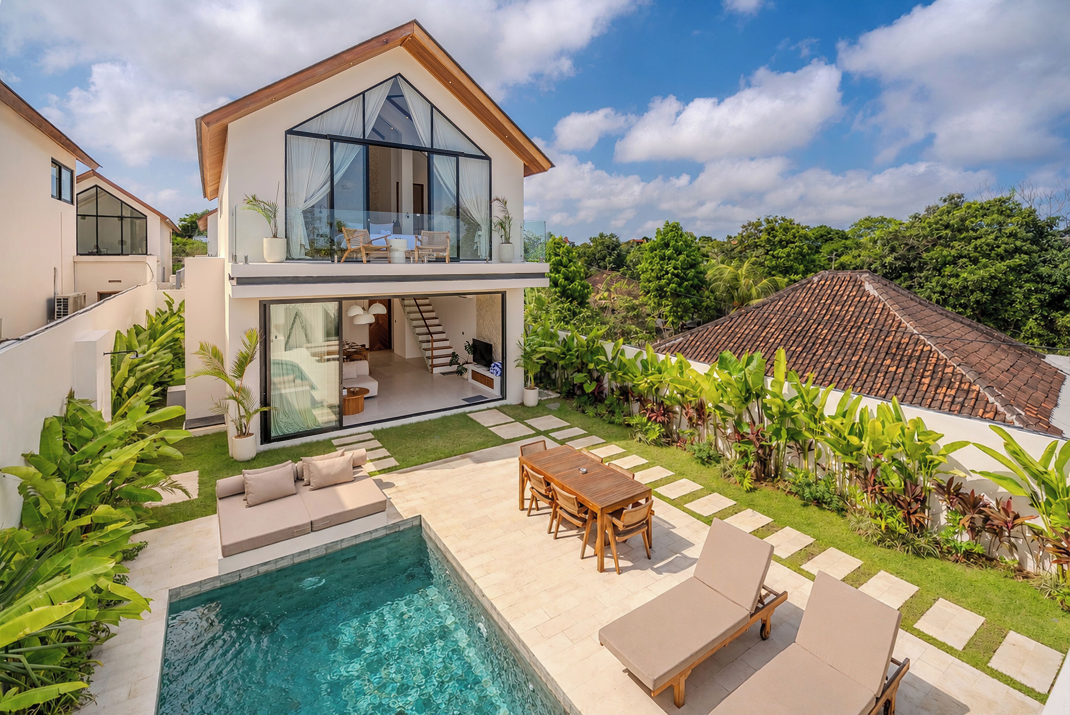 Una casa moderna de dos pisos con piscina, mobiliario de exterior y un jardín exuberante.