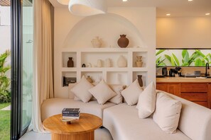 A modern living room with a sectional sofa, a wooden coffee table, and a wall-mounted shelf with decorative vases. - Aintrazy Villa by Betterplace (Unggasan)