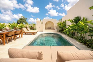 Un área de piscina con sillones, una mesa de comedor y un rincón de estar con cojines.