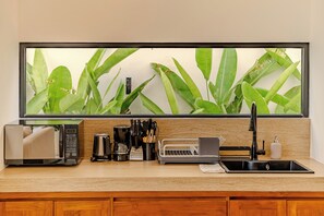 Una cocina con un ventanal grande, cafetera, tostadora y fregadero.