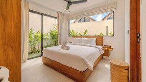 Un dormitorio moderno con una cama grande, un ventilador de techo, un cabecero de madera, una mesita de noche, una cesta tejida y vistas a zonas verdes.