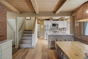 A kitchen with a wooden staircase, a dining area, and a view of the living room. - Round Hill Retreat | Epic Stratton Views w Hot Tub (Winhall)