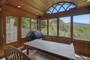 A covered outdoor seating area with a table and chairs, a grill, and a view of the surrounding landscape. - Round Hill Retreat | Epic Stratton Views w Hot Tub (Winhall)