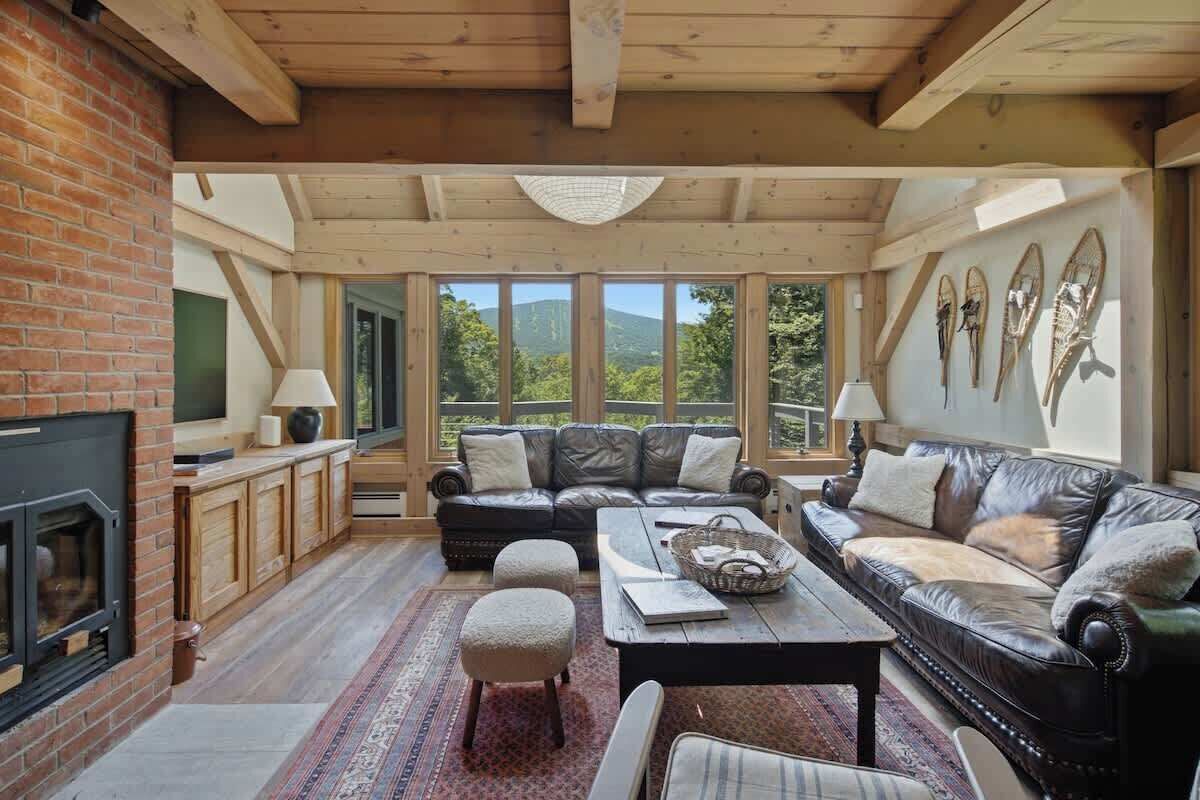 A cozy living room with a fireplace, leather sofas, a coffee table, and a view of the outdoors.