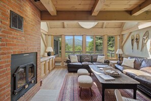 A cozy living room with a fireplace, leather sofas, a coffee table, and a view of the outdoors. - Round Hill Retreat | Epic Stratton Views w Hot Tub (Winhall)