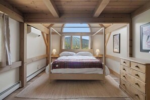 Quarto com teto de madeira, cama com manta xadrez, duas luminárias de cabeceira e uma cômoda.