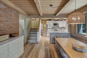 Uma cozinha com mesa de madeira, luminária pendente e parede de tijolos.
