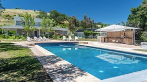 Ein Swimmingpool mit Sonnenterrasse, Liegestühlen und einer Grillgelegenheit.