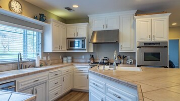 Una cocina con armarios blancos, campana extractora de acero inoxidable, microondas y horno empotrado.