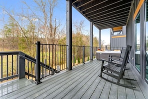 Eine Holzterrasse mit schwarzem Geländer, einer Bank und Blick auf Bäume und ein Gebäude.
