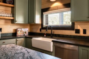 A kitchen with a built-in sink, a window with blinds, and a countertop with a pizza and soup box. - CampingThemed/Pool/HotTub/GameRoom/FirePit/Sleep16 (Sevierville)