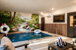 Un espace de bien-être avec une piscine, une fresque représentant un paysage naturel et une porte portant l’inscription « PISCINE ».