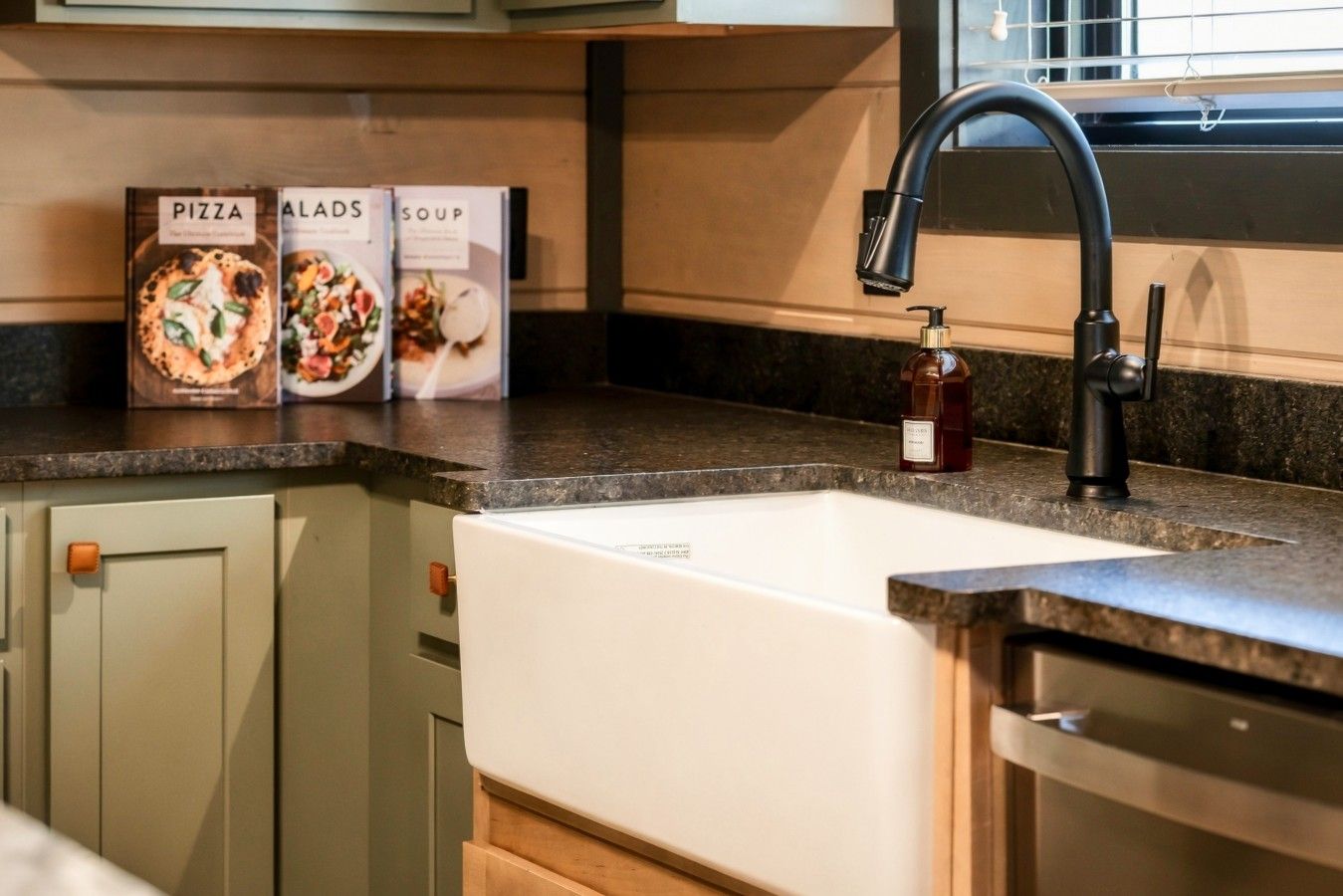 Una cocina con un lavamanos blanco, un grifo negro y tres libros de cocina sobre la encimera.