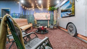 A cozy interior with a sofa, a campfire setup, and a scenic wall mural. - CampingThemed/Pool/HotTub/GameRoom/FirePit/Sleep16 (Sevierville)