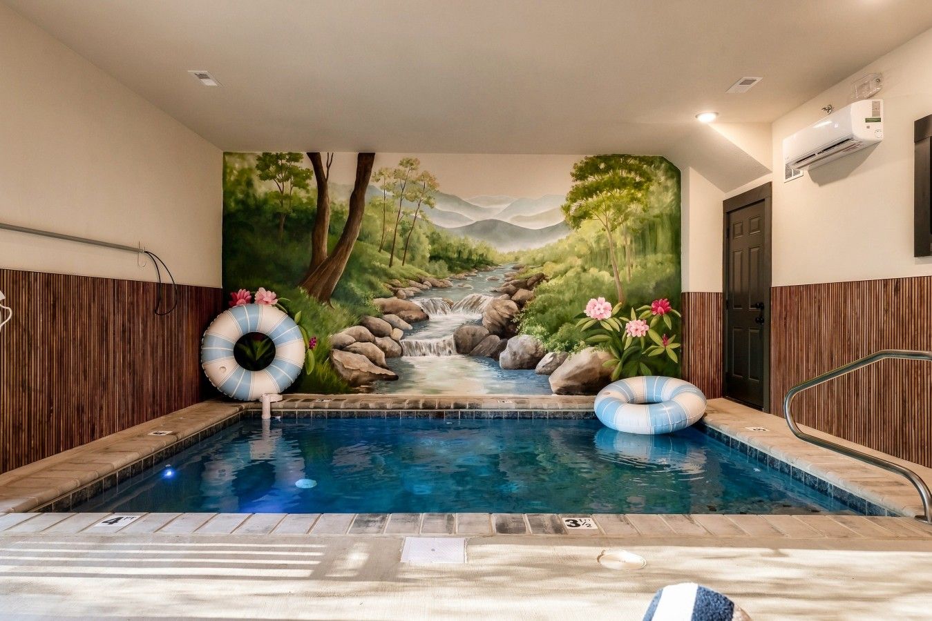 A swimming pool with a mural of a landscape, two inflatable rings, and a door to the right.