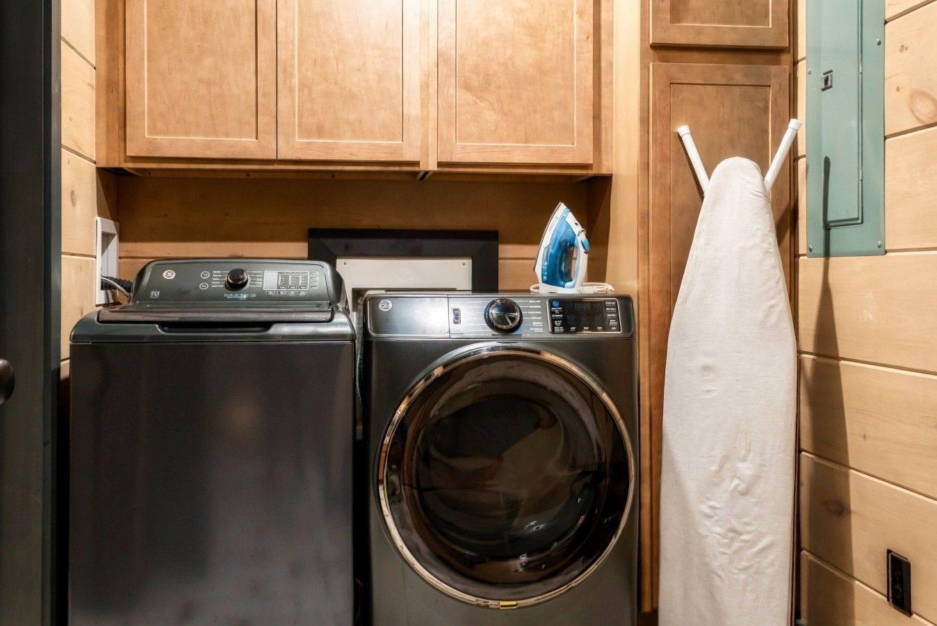 Un espace buanderie compact comprenant un lave-linge et un sèche-linge, des armoires en bois et un porte-serviettes mural.