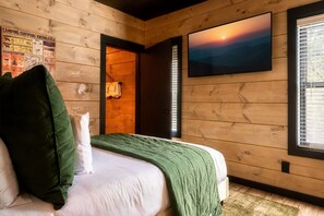 Una camera da letto con un letto, una coperta verde, un cuscino bianco, un poster appeso al muro e un dipinto raffigurante un tramonto.