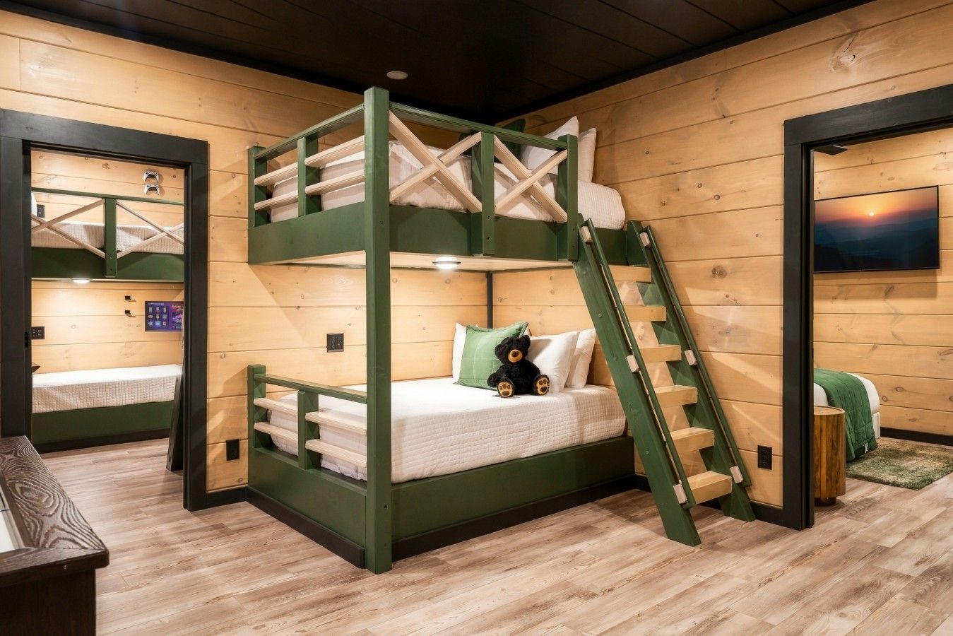 A bunk bed room with a ladder, wooden walls, and a window with a sunset view.