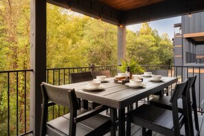 Un'area pranzo all'aperto coperta con un tavolo apparecchiato per quattro persone, circondato da sedie e vista su una zona boschiva.