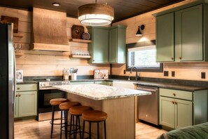 Una cocina con una isla central, taburetes de bar, estufa y armarios verdes.