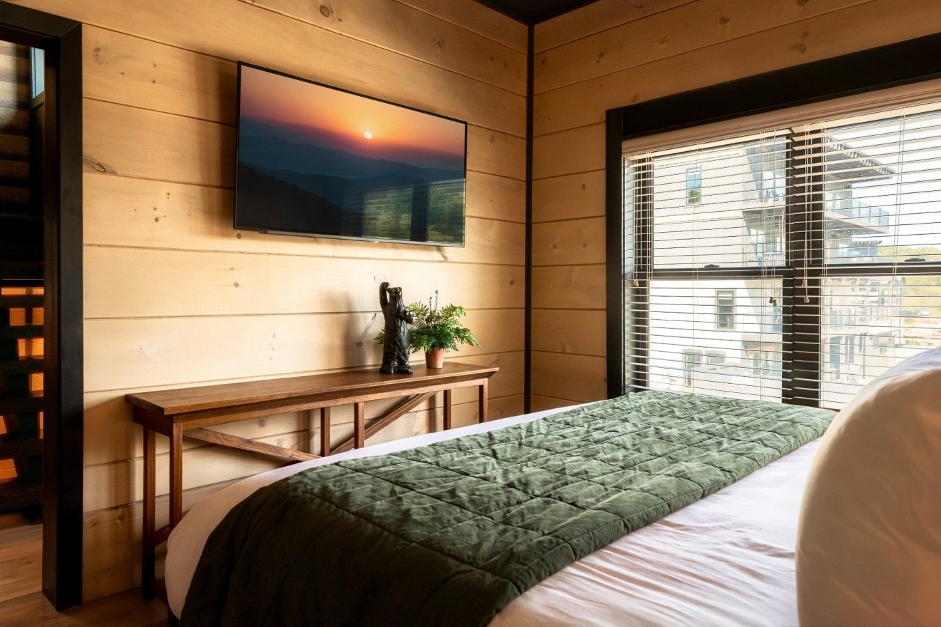 Un dormitorio con una cama, un banco, un cuadro y una ventana con persianas.