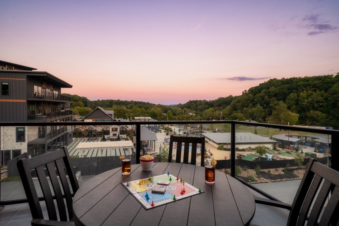 A table with chairs and a board game on a balcony overlooking a pool and buildings.