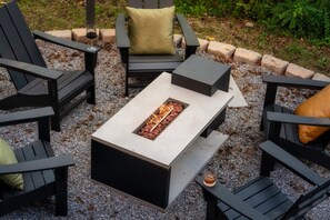 A fire pit table surrounded by black chairs with cushions, set on gravel. - CampingThemed/Pool/HotTub/GameRoom/FirePit/Sleep16 (Sevierville)
