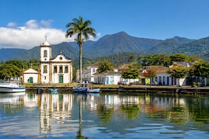 A coastal town with a church, boats, and a mountain backdrop.
